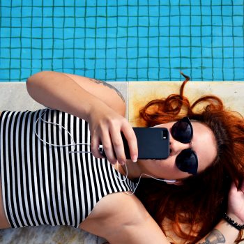 woman laying on the ground taking a selfie by the pool
