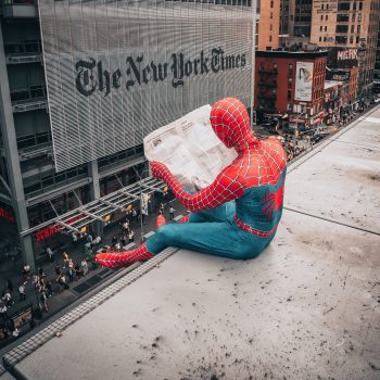 Spiderman sitting on a ledge reading a newspaper by the New York Times building