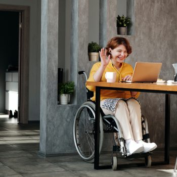 Women in orange top sitting in black wheelchair at a table with a laptop
