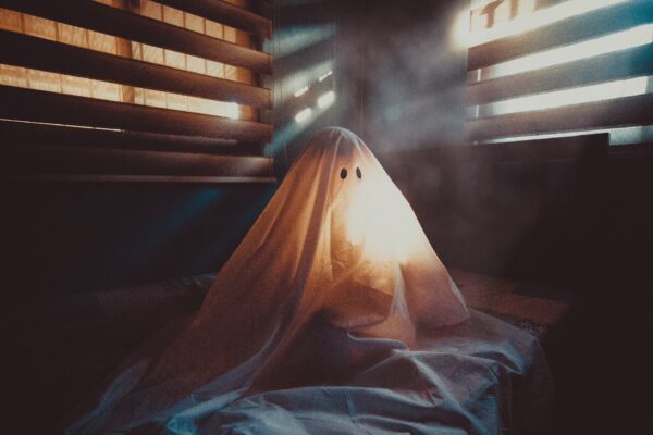 Someone sitting under a "ghost" costume sheet with light coming through the blinds