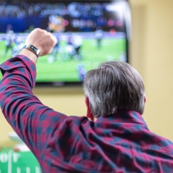 Man sitting on couch cheering at game on TV