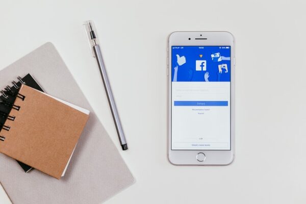Phone displaying Facebook next to notebooks and creative materials