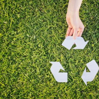 Hand making complete a recycling symbol over green grass