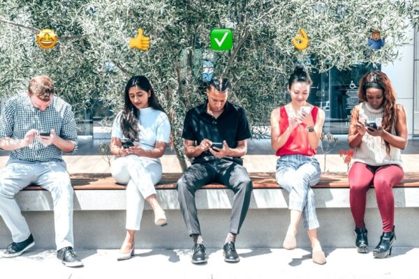 Four people on smartphones with emojis hovering above their heads