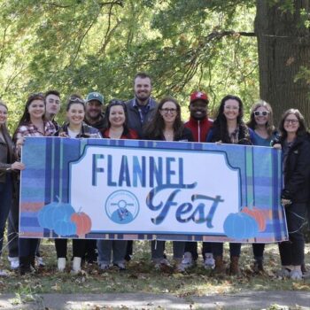 The Scooter Media team posing outside holding a banner that says "Flannel Fest"