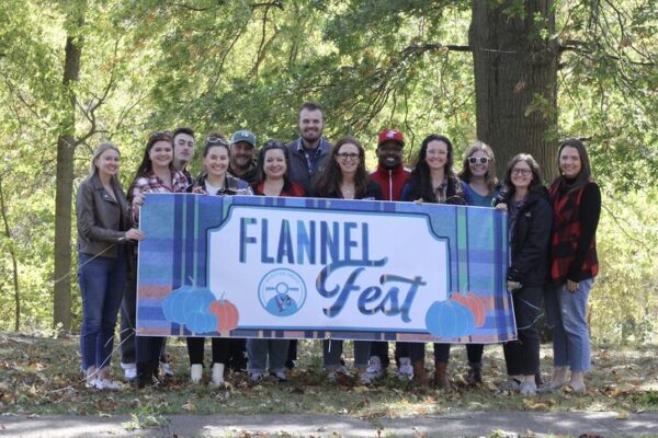 The Scooter Media team posing outside holding a banner that says "Flannel Fest"