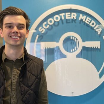 Chase Prather, Assistant Account Executive, standing in front of the Scooter Media logo
