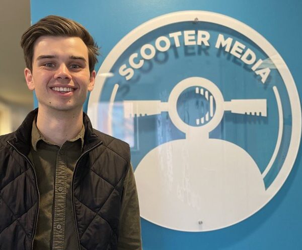 Chase Prather, Assistant Account Executive, standing in front of the Scooter Media logo