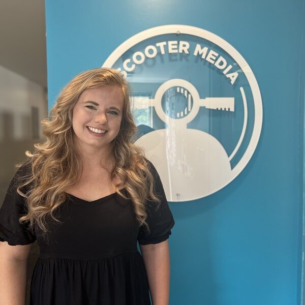 Katie Forcade poses in front of the Scooter Media logo
