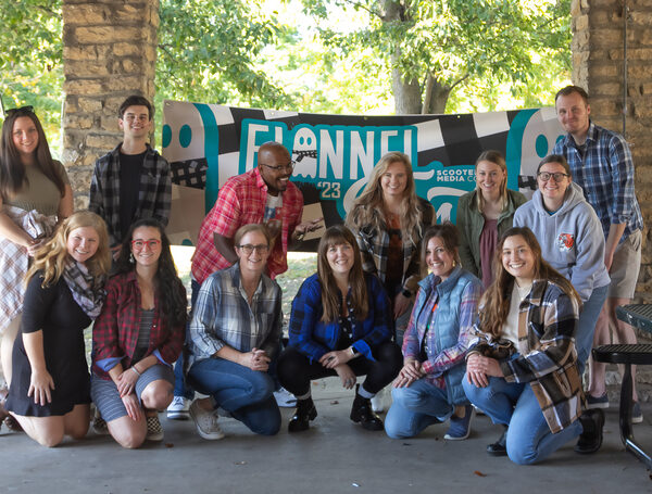The Scooter Media team posing for a photo in front of a teal and black Flannel Fest banner.